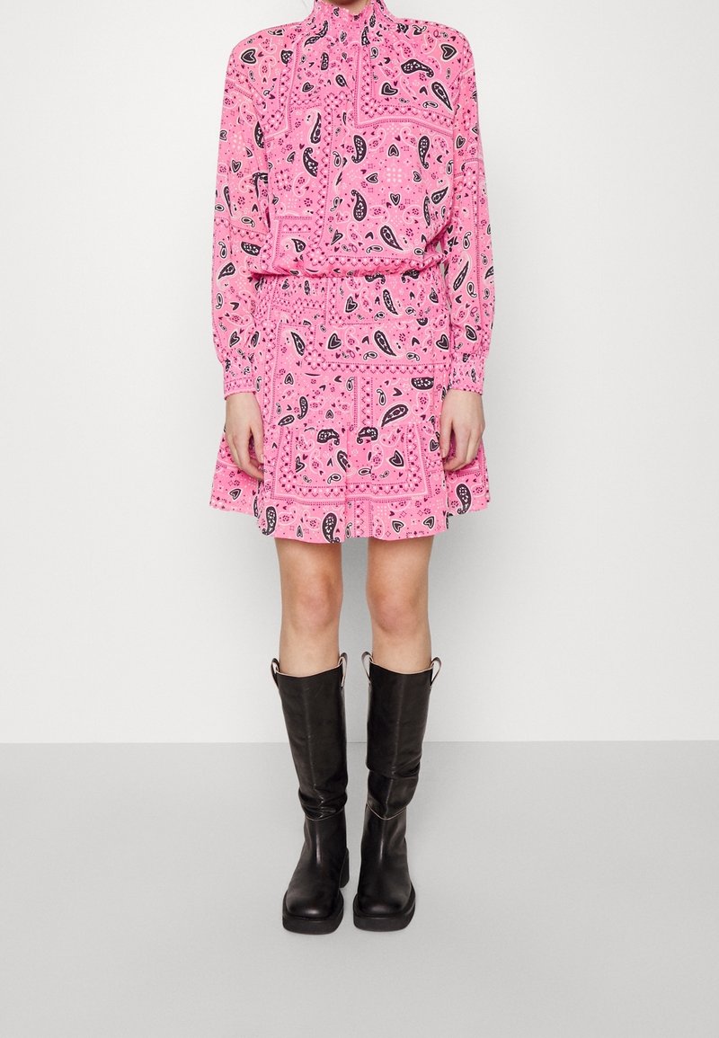 Robe rose ornée de motifs cachemire noirs, avec un col montant et des manches longues, associée à des bottes noires montantes jusqu'aux genoux.