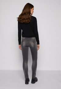 Suéter preto com uma bainha texturizada, combinado com jeans cinza ajustados com bolsos e um acabamento desbotado. Usado com botins pretos.