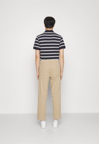 Chemise à manches courtes rayée bleu marine et blanche associée à un pantalon beige ; vue de dos avec des baskets blanches et un design minimaliste.
