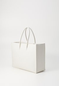 Sac fourre-tout en cuir blanc au toucher lisse, avec des poignées allongées et une forme rectangulaire. Ouvert sur le dessus, avec un design minimaliste et sans matériel visible.