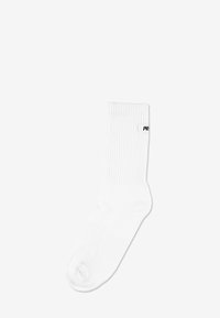 Biała bawełniana skarpetka z prążkowaną fakturą, o długości do połowy łydki, z małym czarnym logo po boku. Gładkie wykończenie, bez wzorów i ozdób.
