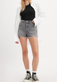 Top de tirantes negro acanalado, pantalones cortos de mezclilla gris con dobladillo deshilachado y camisa de botones blanca de gran tamaño. Zapatillas altas negras con suelas blancas.