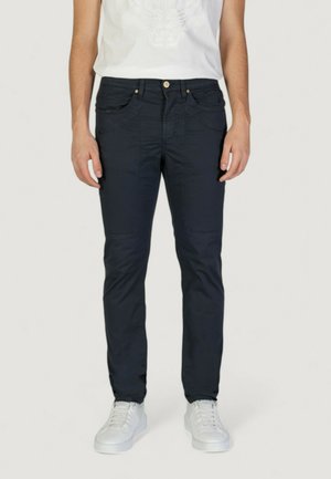 Pantalones oscuros en azul marino, ajustados, con cinco bolsillos, que presentan costuras sutiles y un cierre de botón dorado. Combinados con zapatillas deportivas blancas.