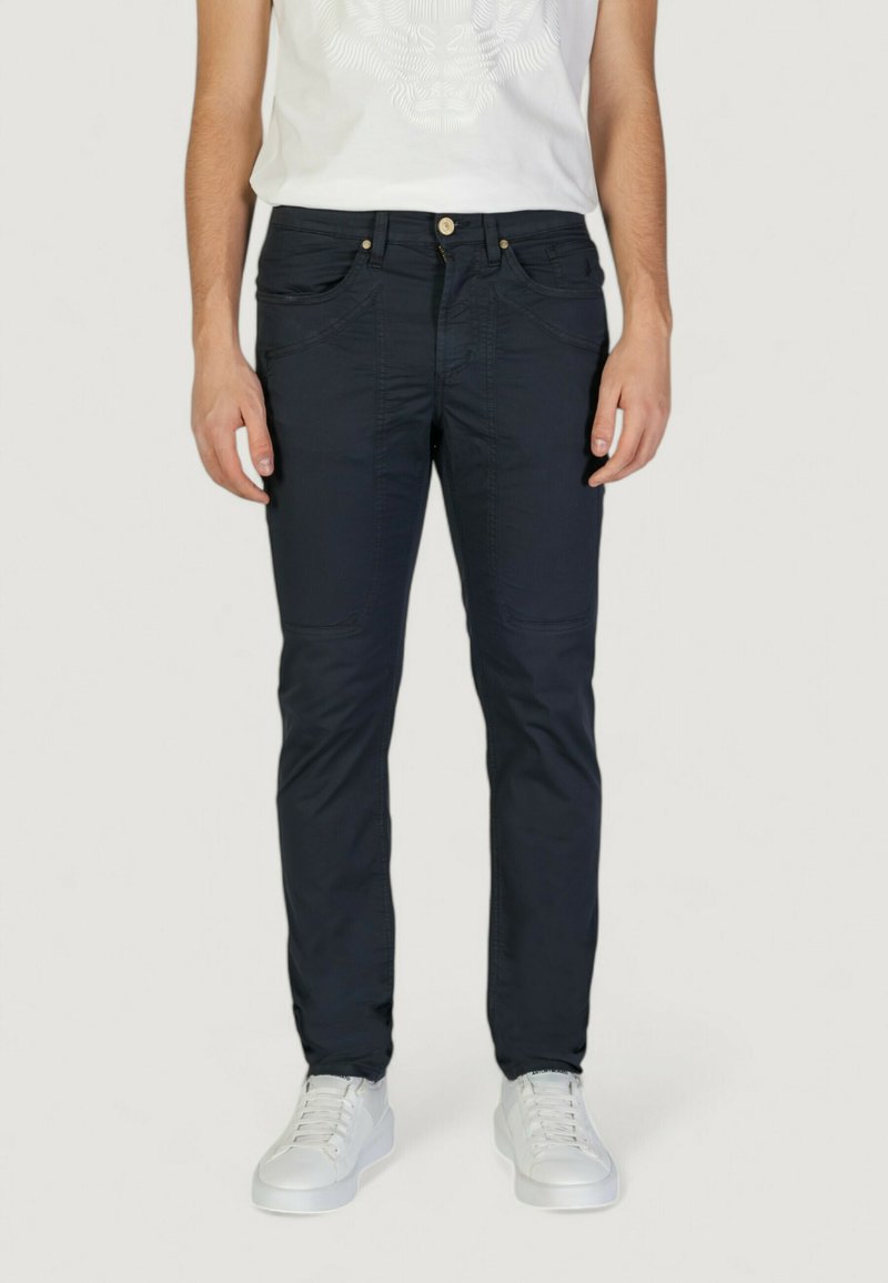 Pantalones oscuros en azul marino, ajustados, con cinco bolsillos, que presentan costuras sutiles y un cierre de botón dorado. Combinados con zapatillas deportivas blancas.