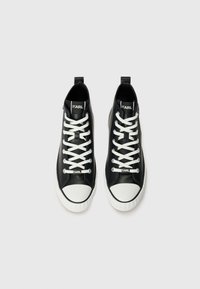 Black high-top sneakers with white rubber toe caps and soles. Features white laces and a logo on the tongue. Smooth leather texture.