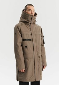 Brązowa ocieplana parka z wysokim kołnierzem, licznymi kieszeniami i regulowanymi sznurkami. Posiada paski na ramionach.
