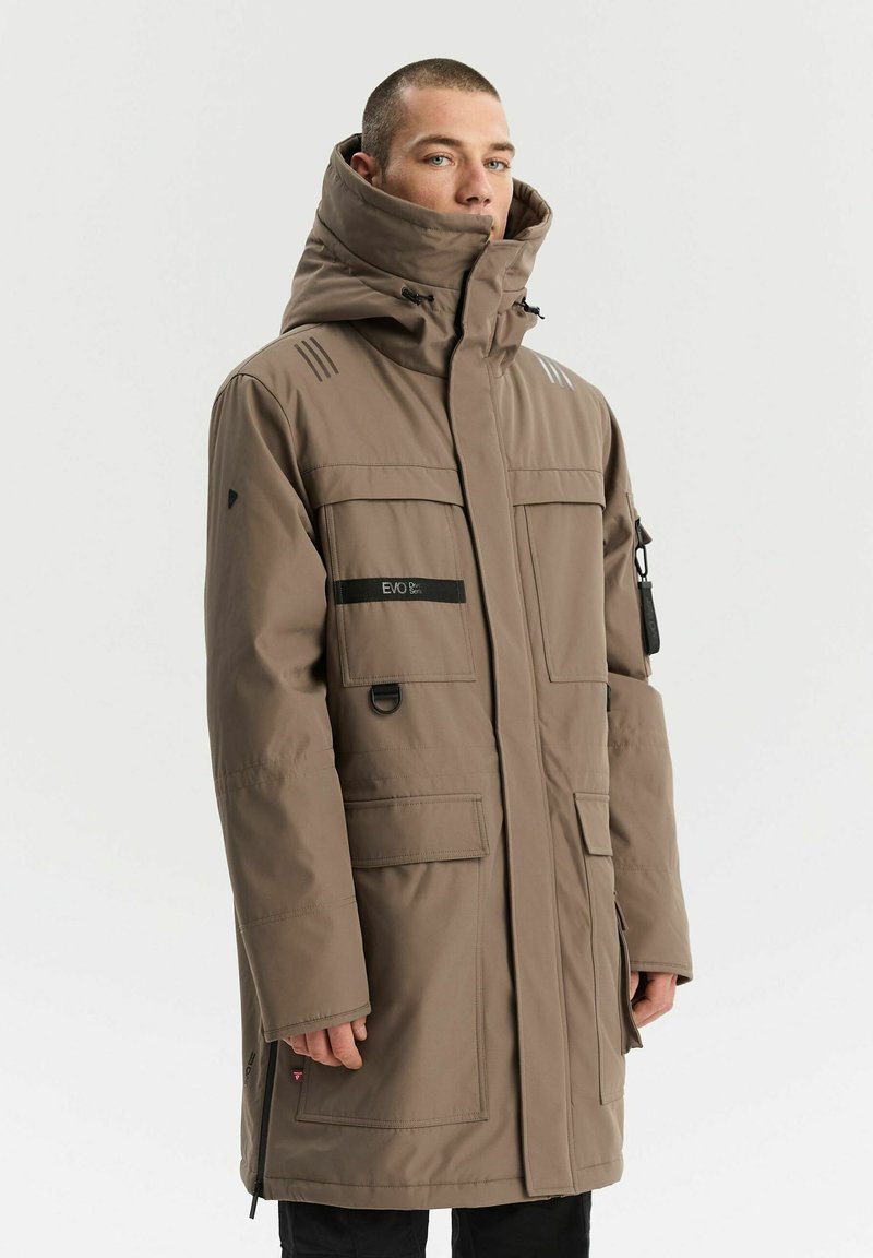 Brązowa ocieplana parka z wysokim kołnierzem, licznymi kieszeniami i regulowanymi sznurkami. Posiada paski na ramionach.