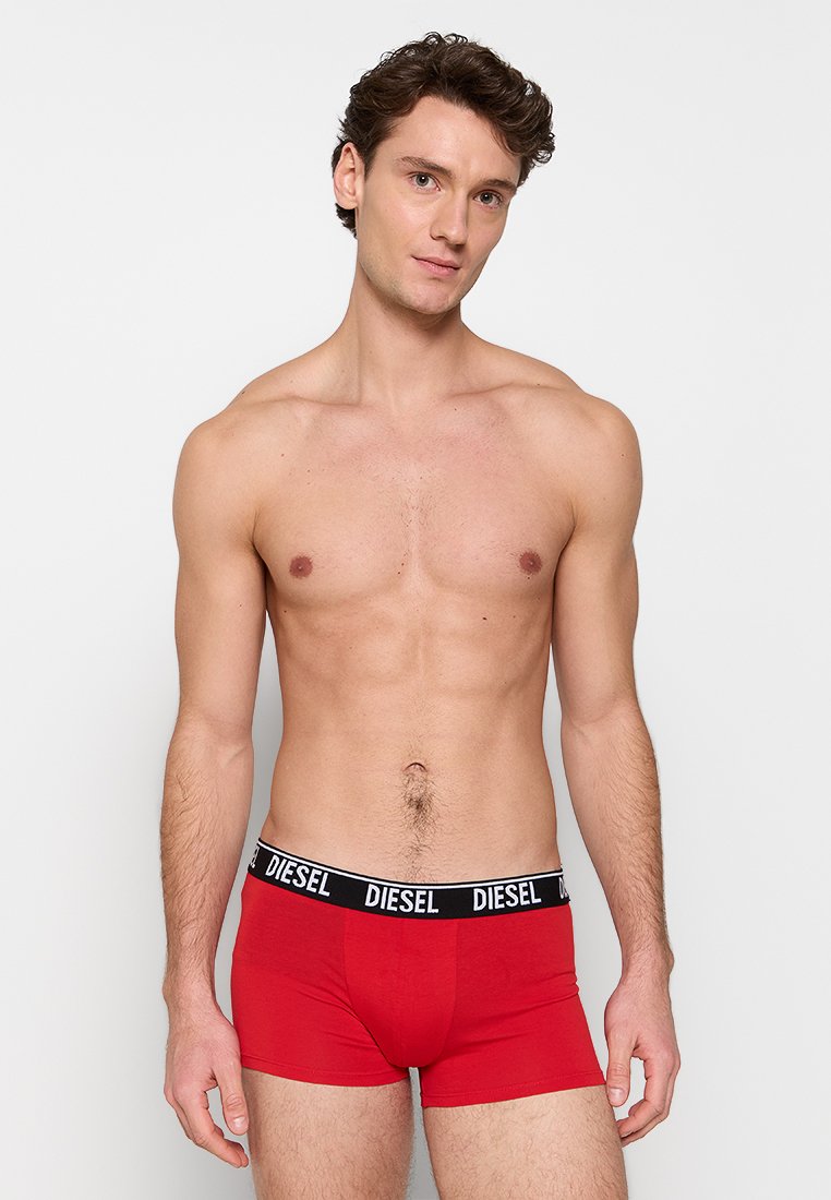 Boxer-briefs en coton rouge avec une taille élastique noire affichant le nom de la marque "DIESEL" en blanc. Texture lisse, design ajusté.