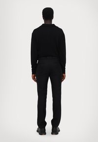 Black long-sleeve polo with a collar, paired with black tailored trousers. Smooth texture, slim fit, and subtle stitching details visible.