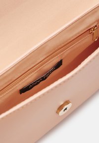 Vaaleanpunainen vegaaninahkainen clutch, jossa on teksturoitu sisustus ja kultainen vetoketju. Sisäpuolella on brändilogo ja erillinen vetoketjullinen tasku.
