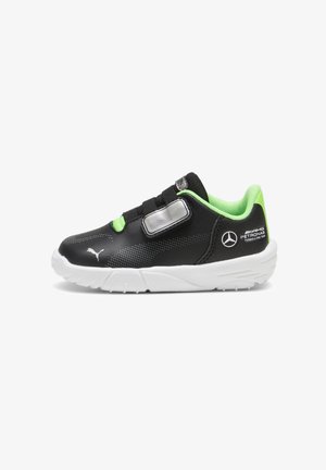 Chaussure de sport noire avec accents verts, tige synthétique texturée, lacets et bride Velcro. Semelle blanche avec détails de marque sur les côtés.
