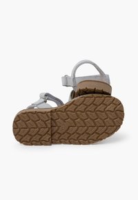 Grijze suède sandaal met meerdere banden, een achterkant met een hielband en een geharde bruine rubberen zool met een profielpatroon voor grip.