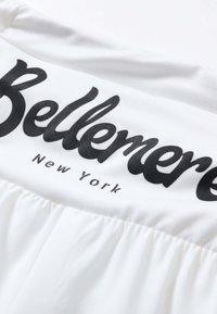 Gros plan d’un vêtement blanc avec le texte noir « Bellemerci New York » imprimé sur un tissu froncé.