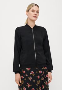 Black bomber jacket with a zip front, round collar, and long sleeves. Made from smooth material, featuring side pockets and a fitted hem.