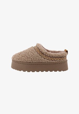 Beige slof met een fluffy, gestructureerde bovenmateriaal en een bruine rubberen zool. Inclusief een decoratieve stiknaad en een kleine hieltab.