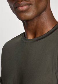Sötétolíva zöld, rövid ujjú póló sima textúrával, kerek nyakkivágással és diszkrét fényességgel, amely kiemeli a testhez simuló fazont.