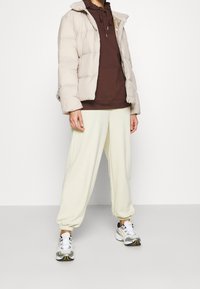 Puffjacka i ljusbeige, brun hoodie under, krämfärgade joggers och grå sneakers med gula detaljer. Bekväm och avslappnad outfit.