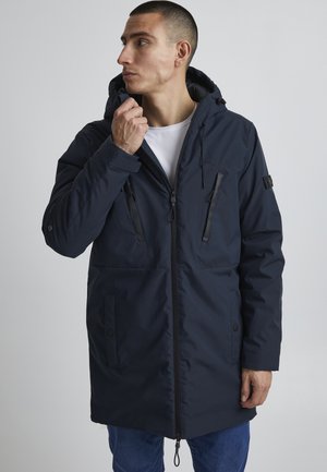 Navy blue parka jacket with a zip front, hood, two front pockets, and black accents. Made of smooth, weather-resistant fabric.