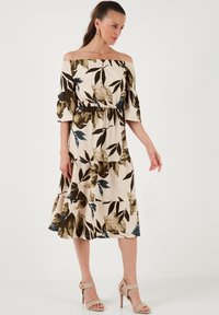 Off-shoulder dress with a fitted waist, featuring a cream base and large dark green and blue leaf patterns. Made of lightweight, textured fabric.