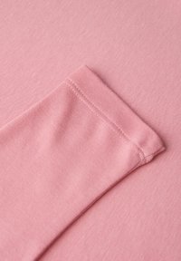 Roze katoen stof van dichtbij, met een gladde textuur en een gezoomde mouwdetail met nette stiksels.