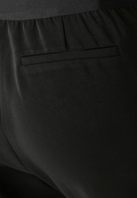 Black fabric pants with a smooth texture and a back pocket detail. The waist features gathered elastic for comfort and fit.