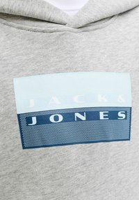 Grey hoodie with a rectangular logo patch featuring the brand name "JACK & JONES" in white and dark blue with dotted patterns.