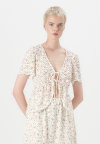Robe à imprimé floral en blanc et couleurs pastel, avec un décolleté en V, des manches bouffantes et un nœud à la taille avec un tissu froncé.