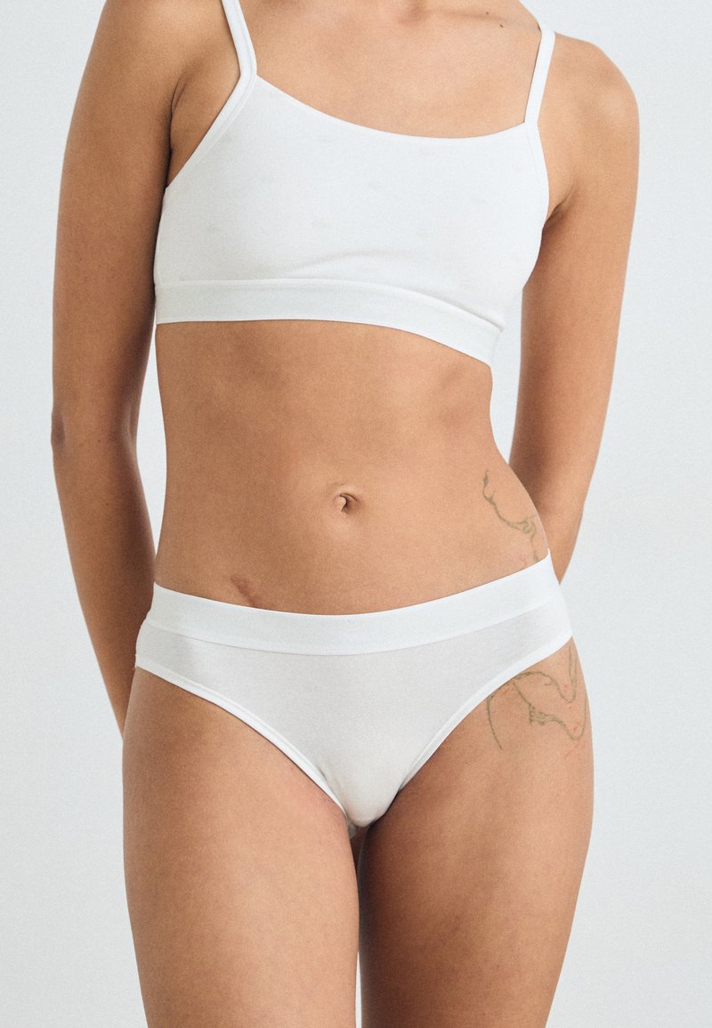 Set di reggiseno e slip in cotone bianco con spalline regolabili, design senza cuciture e texture liscia, caratterizzato da una ampia fascia elastica in vita.