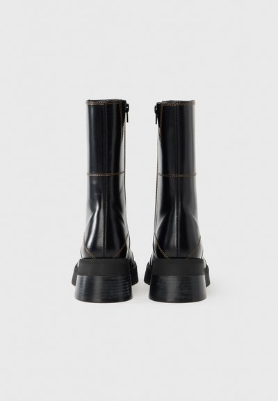 Μαύρα δερμάτινα μπότες έως το γόνατο με χοντρή σόλα, με εμφανείς ραφές και πλαϊνά φερμουάρ για εύκολη εφαρμογή.