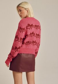 Rosa stickad tröja med ett upprepande mönster av bruna snören, med ribbad fåll och ärmslut. Kombinerad med en figurnära brun läderkjol.