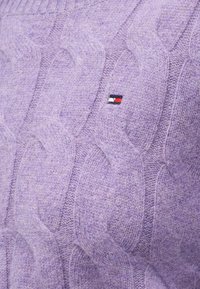 Tessuto a maglia viola con un motivo a treccia che presenta un piccolo logo rettangolare in fili blu navy, bianchi e rossi.