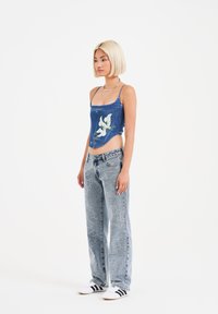 Top corto in denim con ricami floreali; jeans baggy blu chiaro con disegni bianchi a contrasto; abbinati a sneakers in bianco e nero.