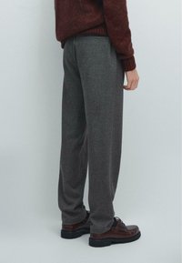 Pantaloni grigi, textured con una vestibilità rilassata, con un design a gamba dritta. Indossati con scarpe in pelle marrone. Vista posteriore, senza dettagli aggiuntivi visibili.