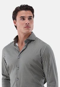 Camicia a righe button-up in verde scuro e bianco; presenta un colletto a punta, una texture liscia e un design aderente con bottoni visibili lungo la parte anteriore.