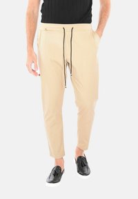 Pantaloni beige con vita elastica e cordoncino nero, tasche laterali, design affusolato e tessuto morbido; abbinati a scarpe nere slip-on.