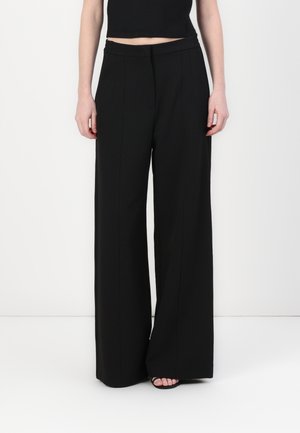 Schwarze, weite Hose mit Falten, aus glattem Stoff, mit elastischem Bund und seitlichen Taschen, auf einem Modell präsentiert.