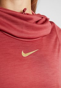 Red t-shirt with a soft, textured fabric and a cowl neckline. Features a gold, glittery Nike logo on the front. Adjustable neck closure.