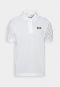 Polo blanc en coton avec col, patte de boutonnage à deux boutons et logo crocodile vert brodé sur la poitrine gauche.