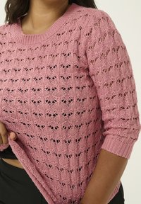 Rosa gestrickter Pullover mit einem zarten Muster aus offenen Maschen, rundem Ausschnitt und gerippten Bündchen. Der Stoff hat eine weiche Textur und ein leichtes Design.