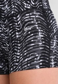 Czarno-szare spodenki sportowe w wzory, z falistymi liniami i gładką teksturą. Posiadają czarne szwy oraz mały akcent logo.