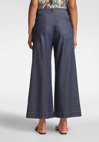 Dunkelblaue, weit geschnittene Jeans mit hoher Taille, zwei Gesäßtaschen und sichtbaren Nahtdetails. Geeignet für legere Outfits.