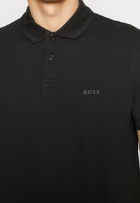 Svart polo skjorta av texturerad tyg, med krage, två knappar och en diskret "BOSS" logo på bröstet.