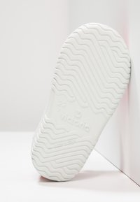Suela de goma blanca de un zapato infantil con patrón de dibujo ondulado, talla 22, marca "Victoria" y "Hecho en España" grabados en la parte inferior.