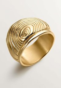Anillo de oro con una textura circular elevada que imita la veta de la madera. La banda lisa resalta el intrincado diseño, mostrando profundidad y un acabado brillante.