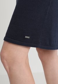 Knit navy blue skirt with a folded hem, featuring a small metal logo tag. Textured fabric with a smooth appearance and relaxed fit.