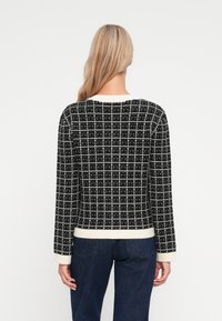 Μαύρο και άσπρο πλεκτό πουλόβερ με σχέδιο σχοινιού, που διαθέτει μακριά μανίκια και άσπρο ριμπ τελείωμα και μανσέτες, εμφανιζόμενο από την πίσω πλευρά.