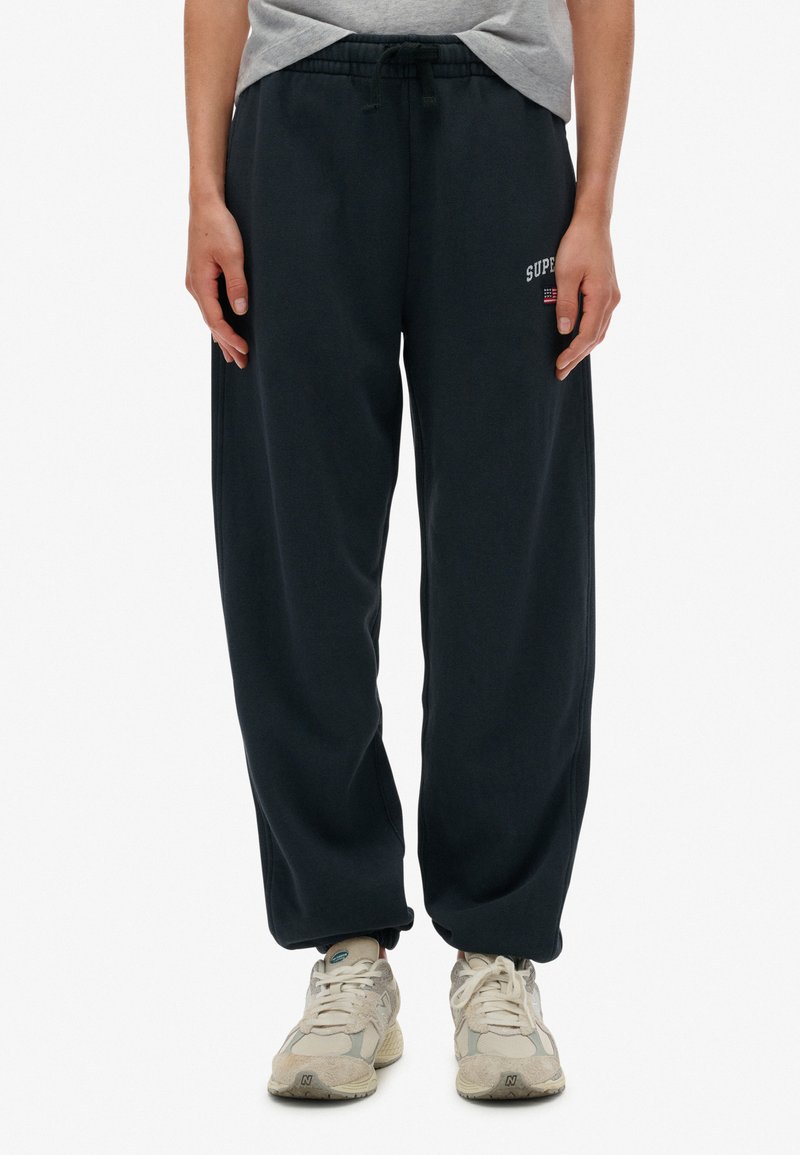 Pantalones de chándal gris oscuro hechos de una tela suave, con cinturilla elástica y cordón, que cuentan con un pequeño logotipo "SUPER" en blanco.