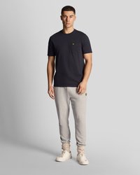 Granatowy t-shirt z krótkim rękawem z kieszonką na piersi, w połączeniu z jasnoszarymi zwężającymi się spodniami dresowymi oraz białymi trampkami z fakturowanym mankietem.