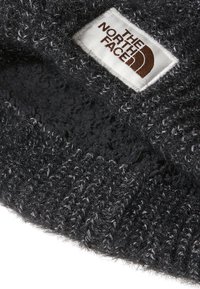 Berretto nero lavorato a maglia con una consistenza pelosa e accenti grigio chiaro; presenta un'etichetta rettangolare bianca con il logo "The North Face".