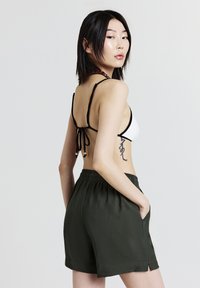 Top bikini bianco e nero con spalline regolabili abbinato a pantaloni corti verde scuro con tasche laterali e vestibilità rilassata, texture liscia.